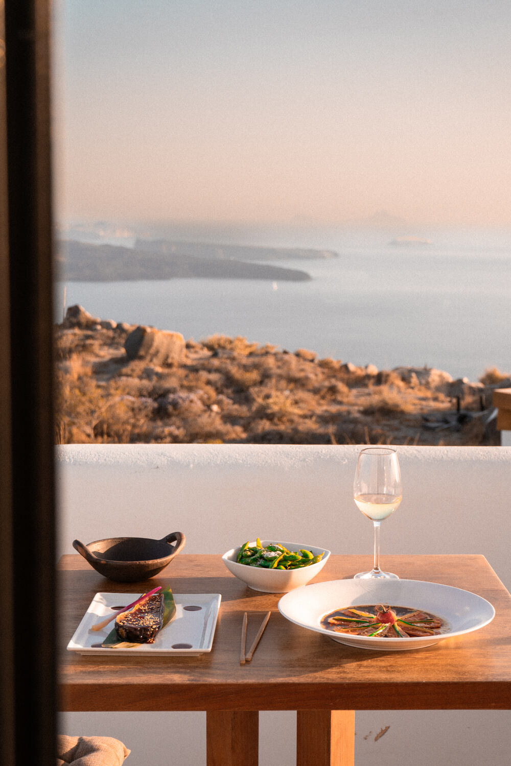 Room service dinner on suite balcony at Nobu Santorini with views out to a sunset sea