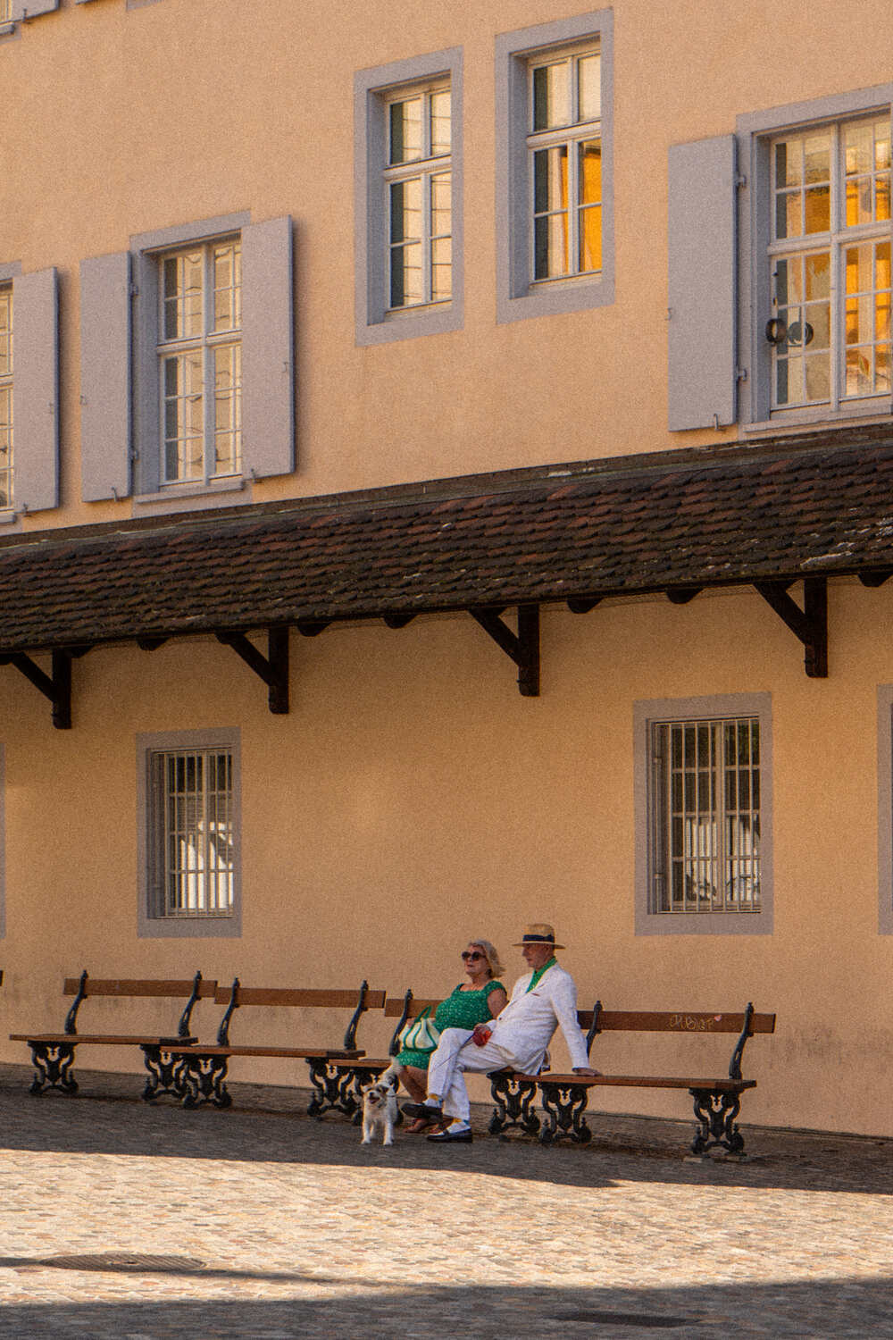 Pastel yellow building in Basel with well-dressed couple sat outside with small dog